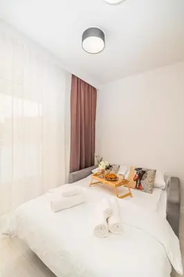 a white bedroom with a large white bed with a table at Prądnik Czerwony Studio - Balcony, City View - by Rentujemy in Kraków