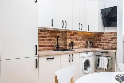 a kitchen with white cabinets and a brick wall at TiB Apartament na Kazimierzu in Kraków