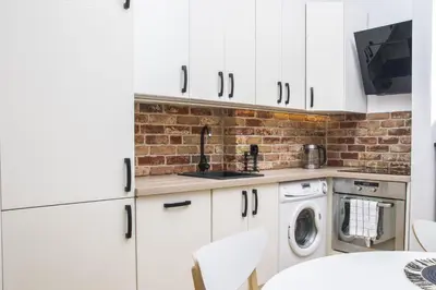 a kitchen with white cabinets and a brick wall at TiB Apartament na Kazimierzu in Kraków