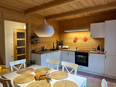 a kitchen with white cabinets and a table with chairs at Sękata Chata - drewniany domek z jacuzzi in Osieczany