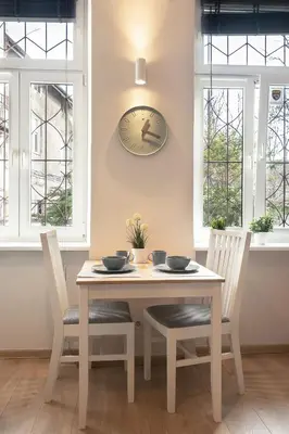 a dining room table with two chairs and a clock on the wall at Enios Apartments Długa 60 in Kraków