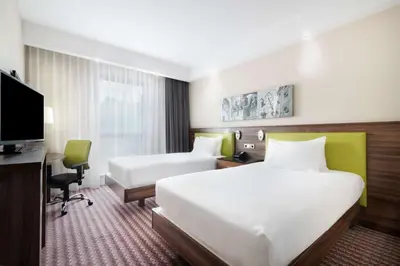 a hotel room with two beds and a desk and a television at Hampton by Hilton Krakow in Kraków