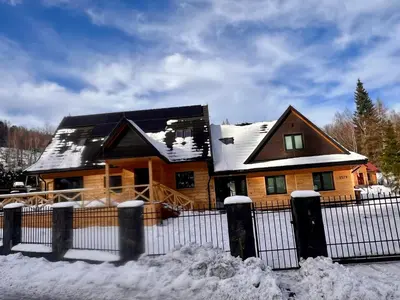a house covered in snow in front of a fence at Dzika Dziura z jacuzzi in Zawoja