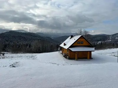 a wooden cabin in the snow with mountains in the background at Domki 15 szczytów in Zawoja