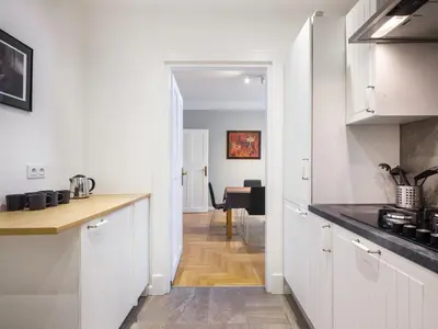 a kitchen with white cabinets and a hallway with a table at Apartments Rynek Glowny in Kraków