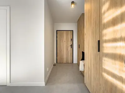 a hallway with white walls and a wooden door at Nowoczesny Apartament Pychowicka 3B in Kraków