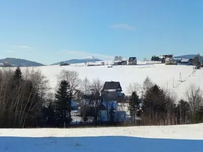 a snow covered field with a house in the distance at Domek pod lasem in Toporzysko