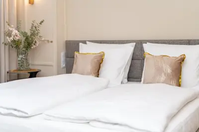 two white beds with pillows and a vase with flowers at Heritage Apartments in Kraków