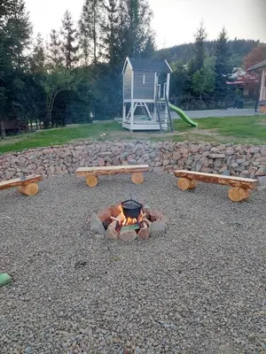 a fire pit with benches and a playground with a house at Plutowka in Zawoja