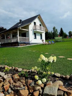 a white house with a porch and a rock garden at Plutowka in Zawoja