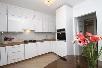 a kitchen with white cabinets and pink flowers in a vase at Apartament Słowackiego in Oświęcim