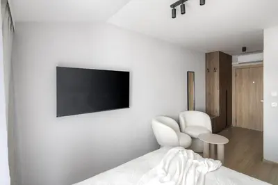 a bedroom with a tv on the wall and two white chairs at Iron Street by A11 Sauna in Kraków
