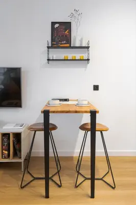 a table with two stools and a shelf on the wall at Bright and cosy flat near the river in Kraków