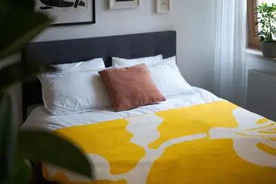a bed with a yellow and white blanket and pillows at Bright and cosy flat near the river in Kraków