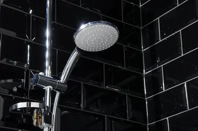 a shower head in a bathroom with black tiles at Cracow Fancy Brick #1 - Old Town in Kraków