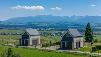 two houses in a field with mountains in the background at Domki z Widokiem Klikuszowa jacuzzi in Klikuszowa