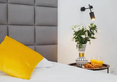 a bed with a yellow pillow and a vase of flowers and orange juice at Golden Honey Apartments in Kraków