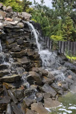 a waterfall on a stone wall next to a pond at Zajazd Pasja in Sławków