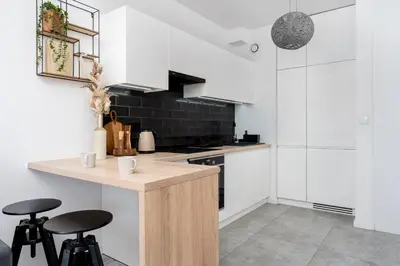 a kitchen with white cabinets and a counter with stools at Malila Premium Apartments Cracow Konopnickiej 63E in Kraków