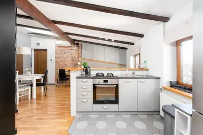 a kitchen with white cabinets and a dining room with a table at Park Krakowski Loft Apartment by BookingHost in Kraków