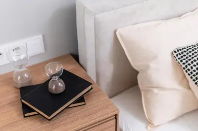 a bedside table with an alarm clock and glasses on it at Sandstone Apartament - homfi Collection in Kraków
