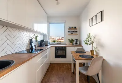 a kitchen with white cabinets and a wooden table at Zoya Apartament in Kraków