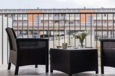 two chairs and a table with a vase of flowers on a balcony at Nowoczesny Apartament w Krakowie z Klimatyzowanym Salonem Dwa Miejsca Postojowe by Noclegi Renters in Kraków