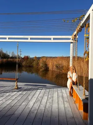 two women sitting on a dock next to a river at Raj na Hektarach in Wysokie