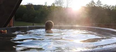 a man in a hot tub with the sun in the background at Wiśniowe Zacisze - Agroturystyka in Sułkowice