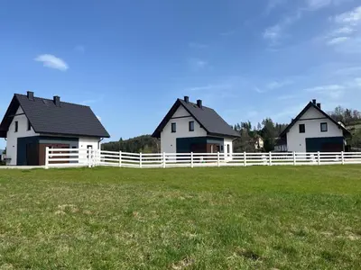 two houses in a field with a white fence at Agroturystyka Nad Lasem - Domki w górach in Toporzysko