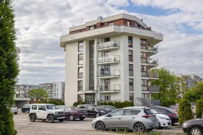 a tall white building with cars parked in a parking lot at Żabiniec Stylish Apartment in Cracow with Balcony by Noclegi Renters in Kraków