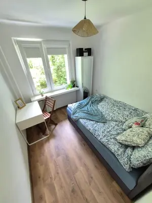 a bedroom with a bed and a desk and two windows at Dąbie Park Apartament in Kraków
