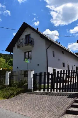 a white house with a black fence at Pokoje pod Śnieżnicą in Kasina Wielka