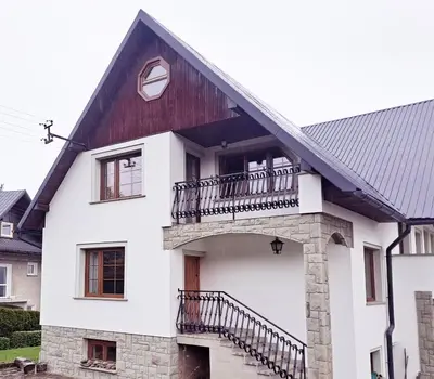 a white house with a black roof and a balcony at Mars 5 in Limanowa