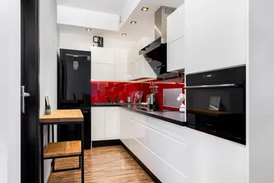 a kitchen with red and white cabinets and a wooden floor at Komorowskiego Riverside Apartment by BookingHost in Kraków
