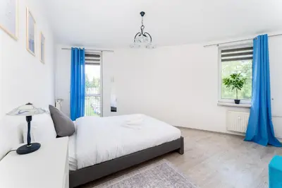 a white bedroom with blue curtains and a bed at Osiedle Oświecenia Comfort Apartment by BookingHost in Kraków