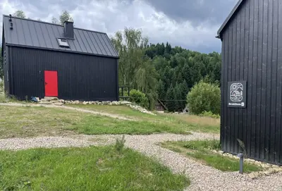 a black barn with a red door in a field at BeskiDom in Zawoja