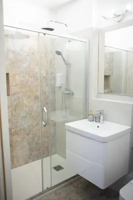 a white bathroom with a shower and a sink at Apartments Roman in Kraków