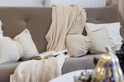 a blanket on a couch with a book and pillows at Malila Premium Apartments Łaszkiewicza 8 -Tauron Arena Parking in Kraków