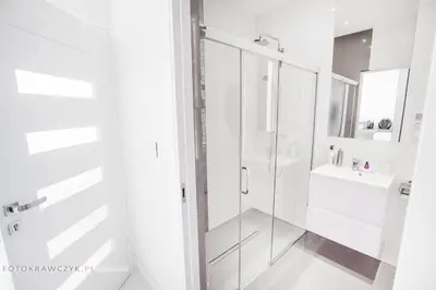 a white bathroom with a shower and a sink at Apartament Nadwiślańska in Kraków