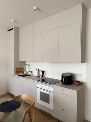a kitchen with white cabinets and a table and a chair at Olszańska Gem in Kraków
