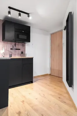 an empty kitchen with black cabinets and a wooden floor at Househost Apartment Plac Wolnica 9 in Kraków