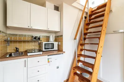 a kitchen with white cabinets and a wooden staircase at RentPlanet - Apartament Garbarska in Kraków
