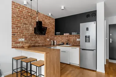 a kitchen with a brick wall and a counter with stools at Cricoteque Residence - Luxury 1BR Riverside Suite in Kraków