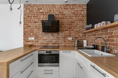 a kitchen with white cabinets and a brick wall at Cricoteque Residence - Luxury 1BR Riverside Suite in Kraków