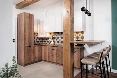 a kitchen with wooden cabinets and a bar with stools at The Vitrail Apartments - by Upstairs in Kraków