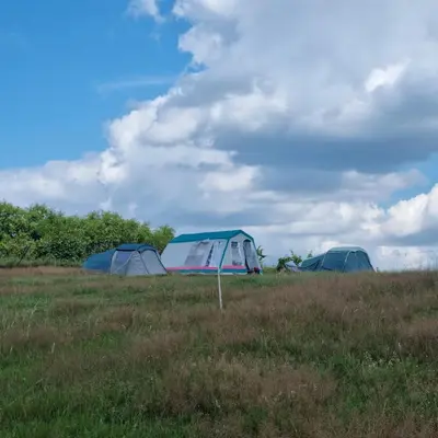three tents in a field with a cloudy sky at Uszate Ranczo Jagoda in Rybna