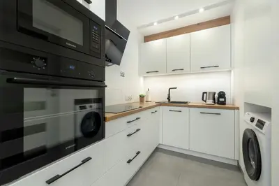 a kitchen with white cabinets and black appliances at Cosy Apartment in Cracow with Parking, Desk and Balcony by Noclegi Renters in Kraków