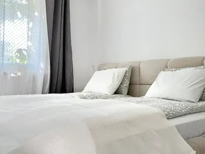 a bed with white sheets and pillows next to a window at Cozy Apartment 10 minutes to Wawel Castle in Kraków
