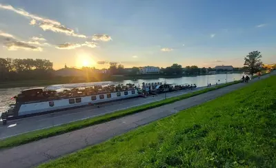 a boat on a river with the sunset in the background at Apartment next to Wawel, Premium Stay in Central Krakow by Koletek 3 in Kraków